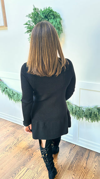 The Nikita Dress — black drop-waist sweater dress with ruffle accents